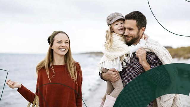 En familie på 3 går smilende på stranden