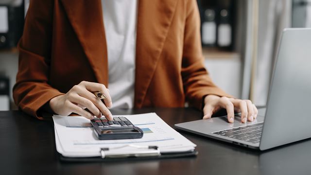Person bruger lommeregner og udfylder dokument ved siden af en bærbar computer.